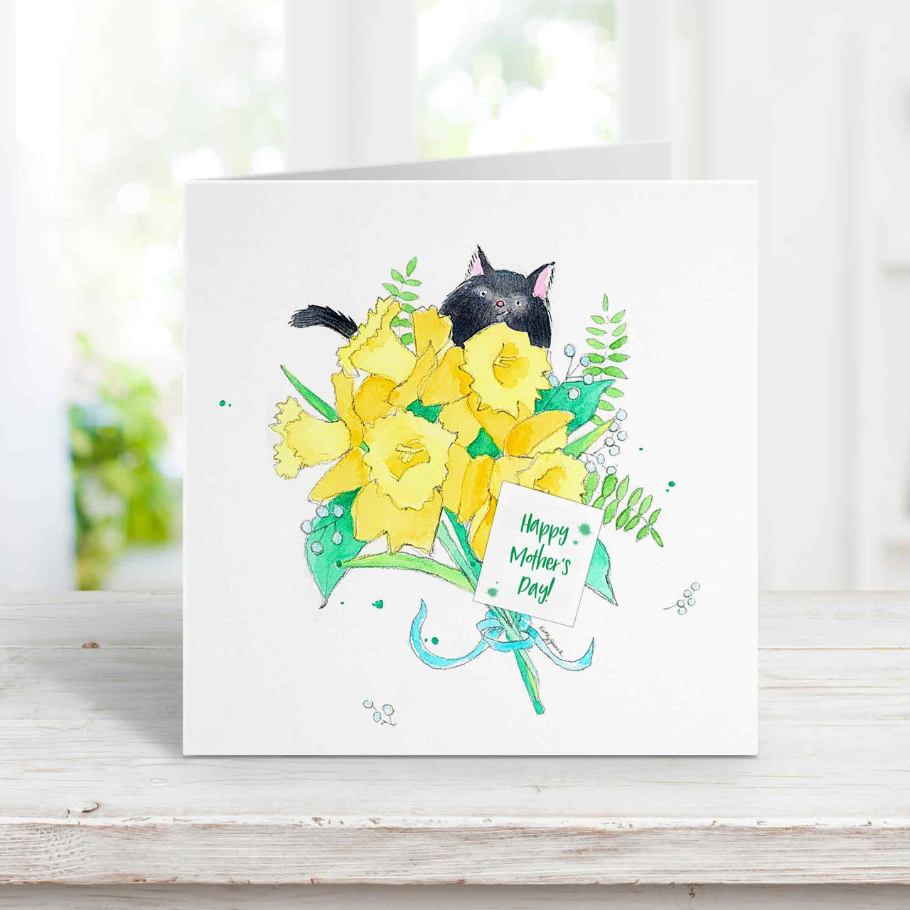 Mothers day card with a whimsical black cat peeking out behind a bouquet of yellow daffodils. There is a small white tag that says Happy Mothers Day.