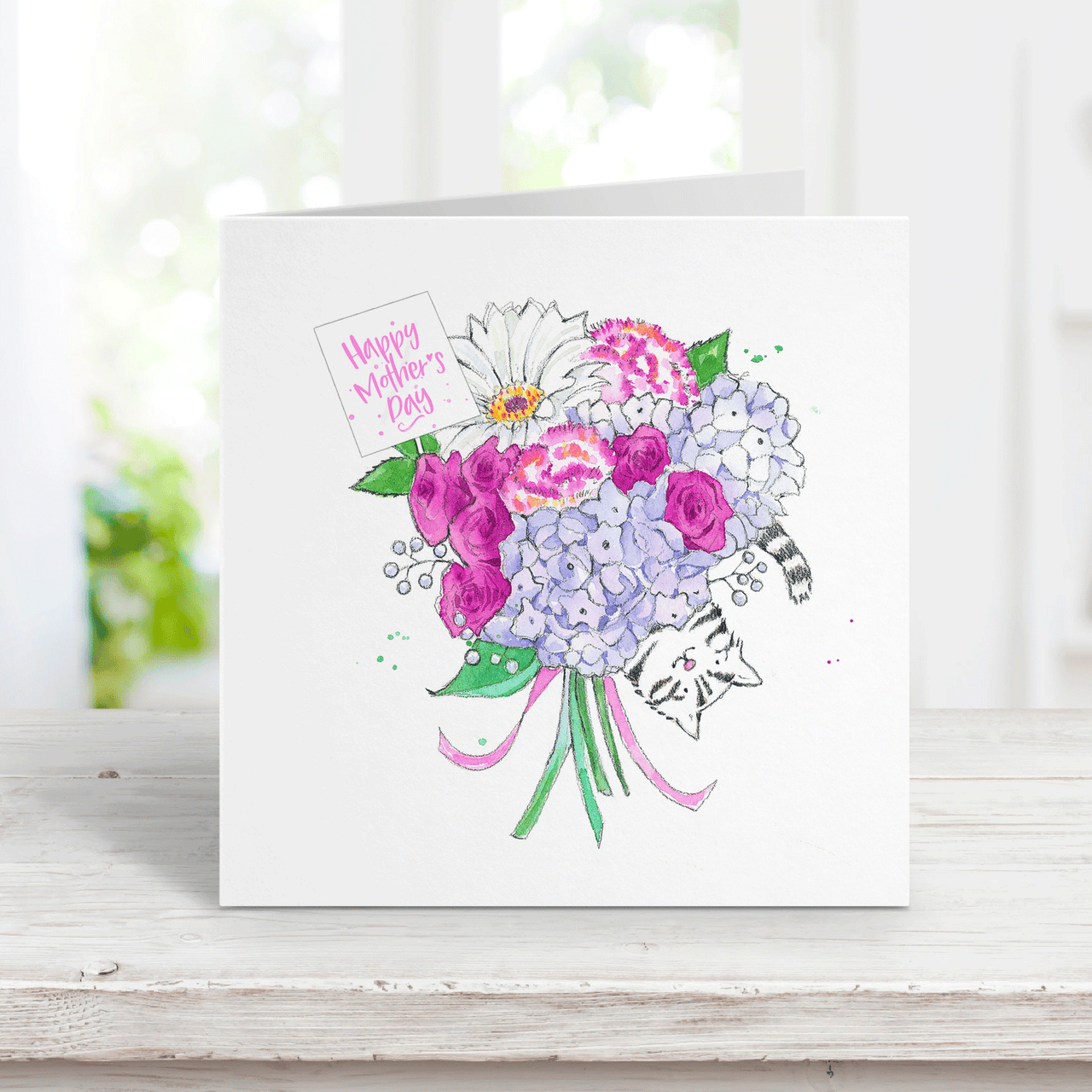A watercolor card with a gray tabby cat peeking out behind a bouquet of purple flowers with a small tag that says Happy Mothers Day
