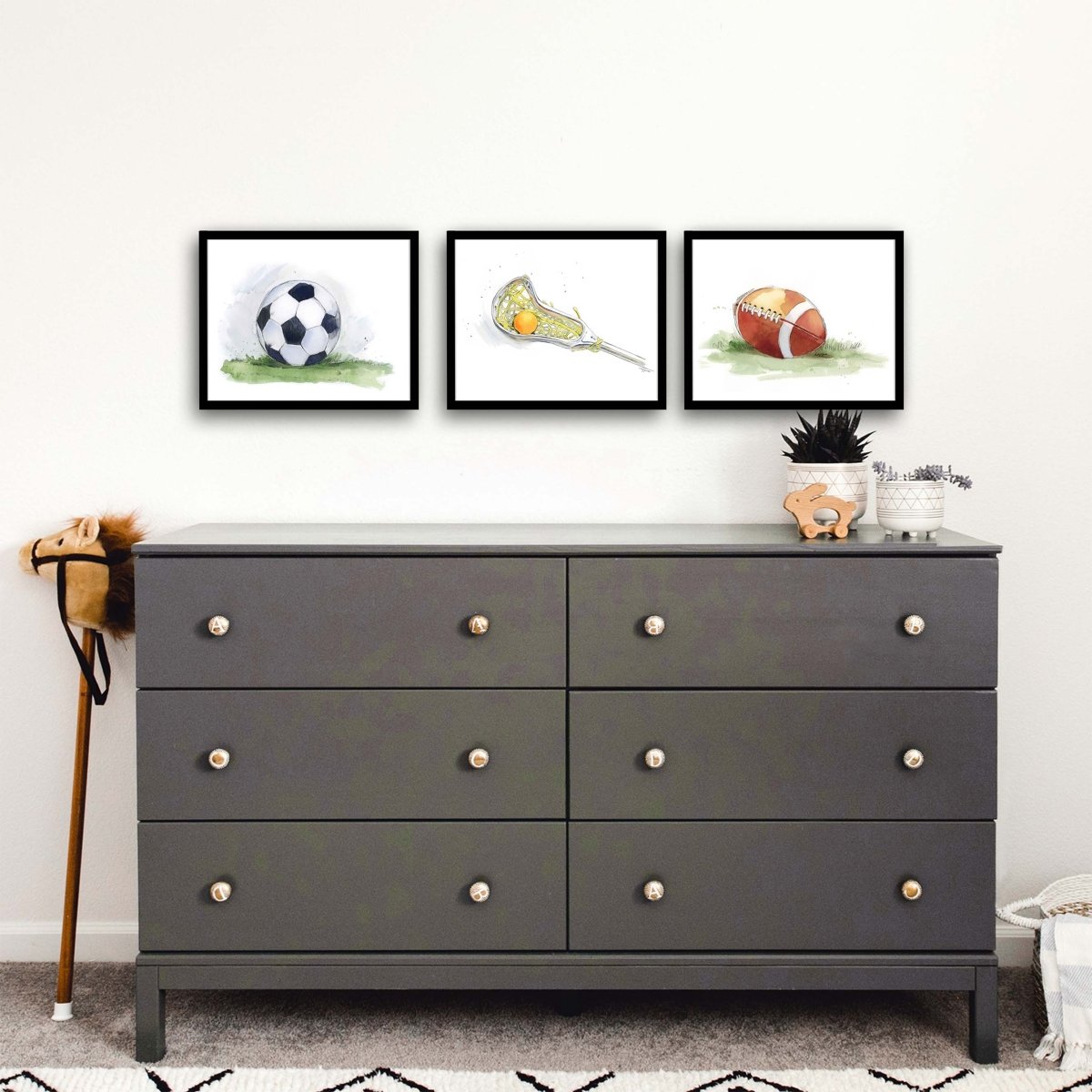 Three framed prints of soccer ball, lacrosse stick and ball and football in a boys room.